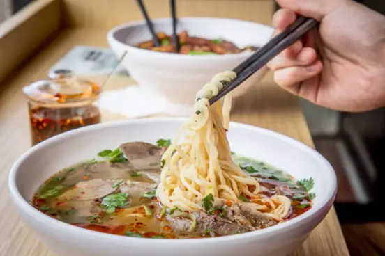 Hand with chop stix eating bowl of Magic Noodles