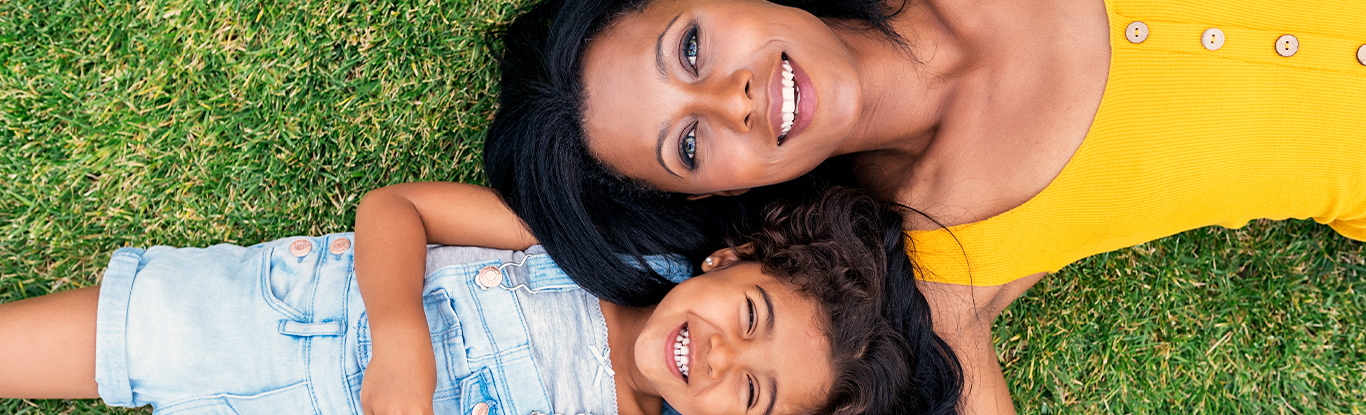 a woman and small child laying on grass as smiling