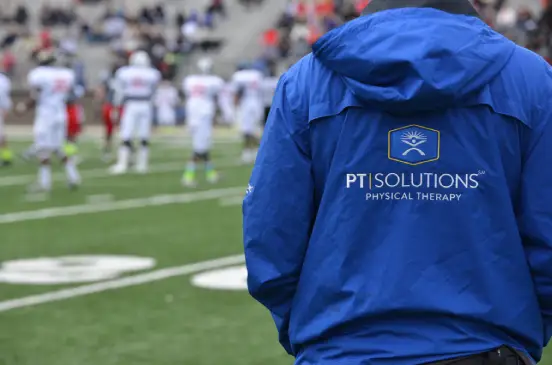 Man in PT Solutions jacket watching football